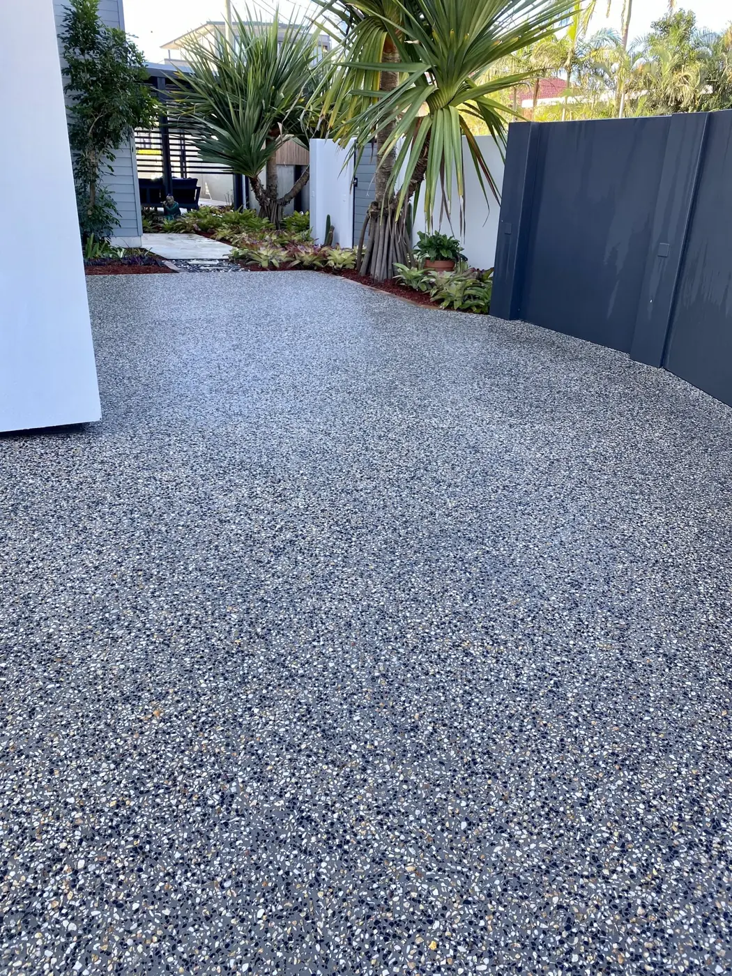 Dark exposed aggregate driveway beside a charcoal fence