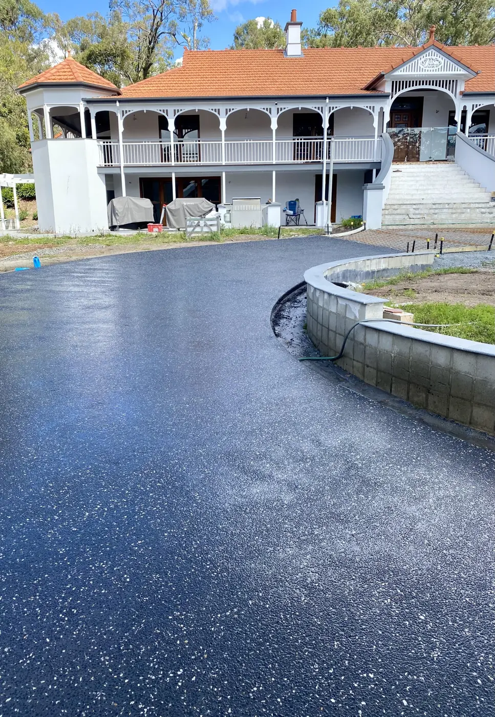 Freshly sealed dark exposed aggregate driveway curving up to a Queenslander