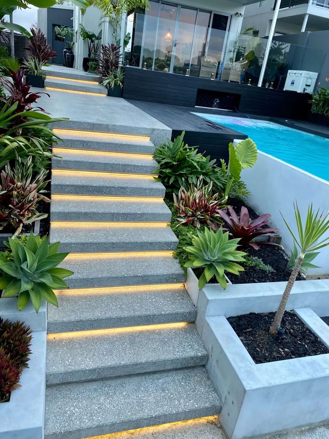 Floating concrete stairs with LED strip lighting beside a pool